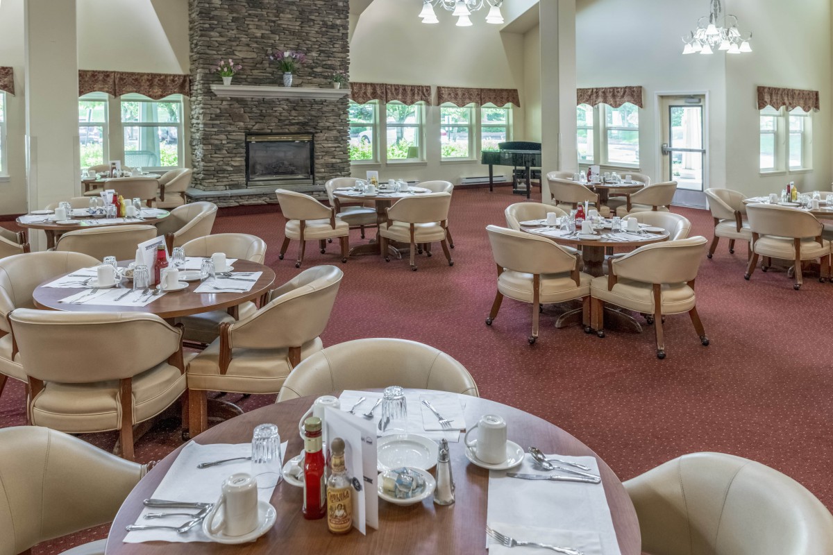 A spacious dining room with neatly arranged tables and chairs, featuring a fireplace and large windows.