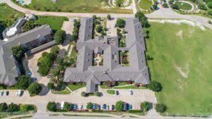 An aerial view of a large building with surrounding greenery and a parking lot.
