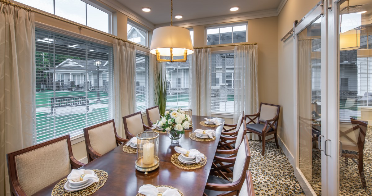 An elegant dining room with a large table set for a meal, surrounded by chairs and illuminated by a chandelier.