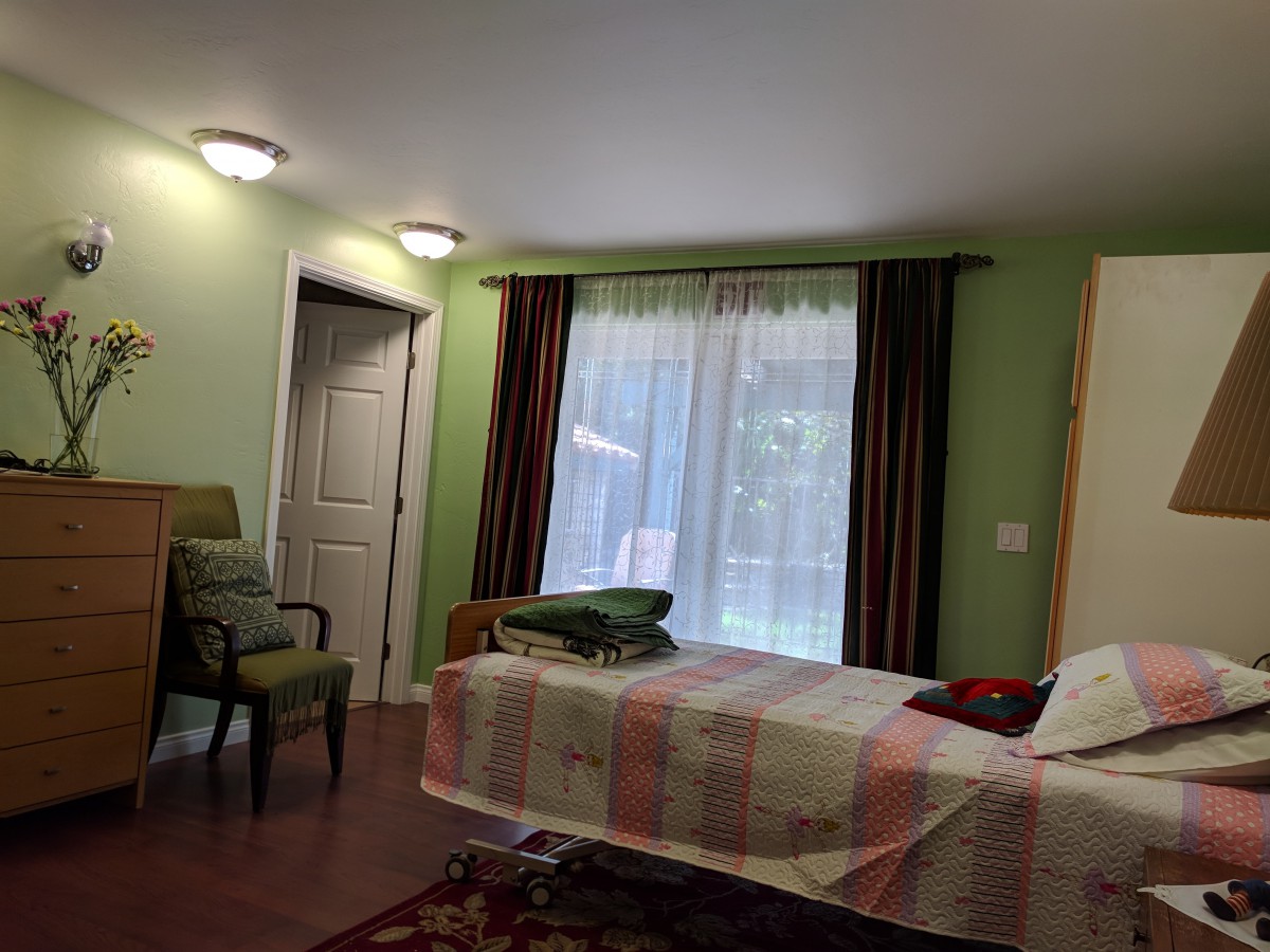 A cozy bedroom with a neatly made bed, chairs, and large window with curtains.