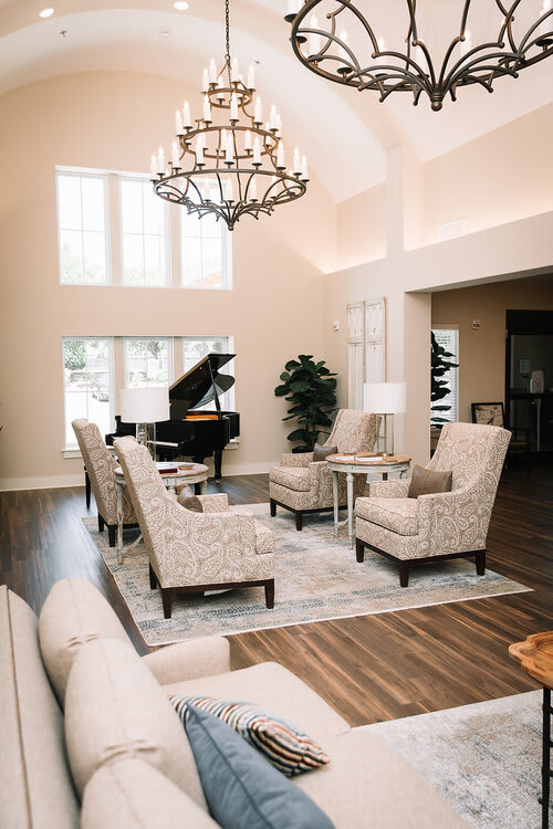 A modern living room featuring elegant furniture and a grand piano under a large chandelier.