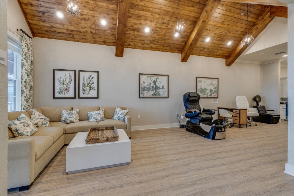 A spacious living room features a cozy seating area, massage chair, and modern decor under wooden ceiling beams.
