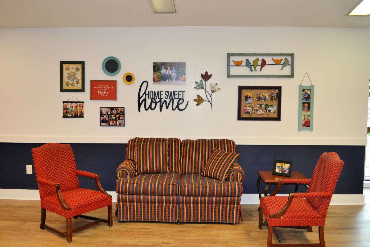 A cozy living room with a striped couch, two red armchairs, and a wall adorned with various artworks.