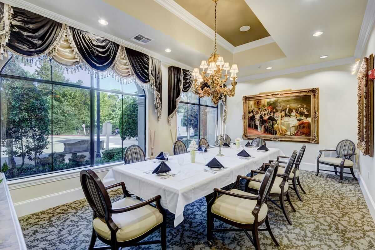 An elegant dining room with a long table set for guests, featuring a chandelier and sophisticated decor.