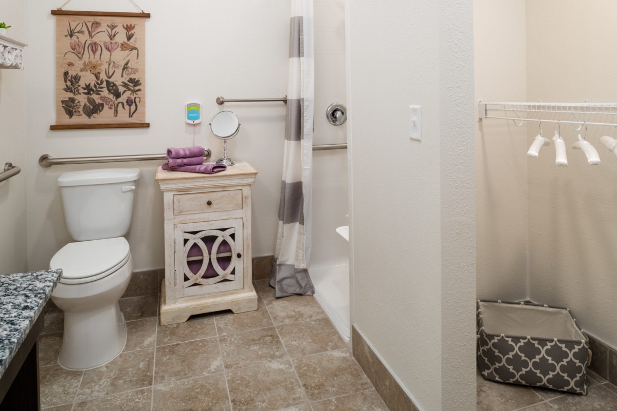 A neatly organized bathroom featuring a toilet, a shower with a curtain, and a small cabinet with towels.