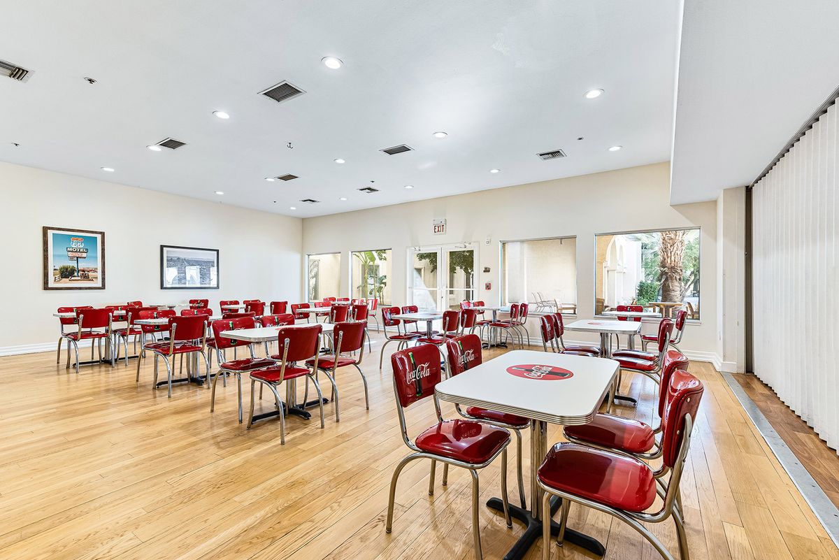A spacious dining room with red chairs and tables arranged neatly on a wooden floor.
