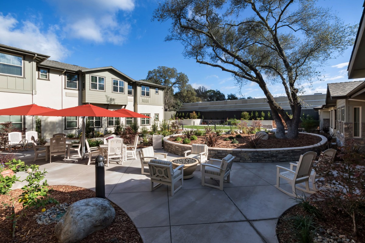 A sunny outdoor patio area with seating and a residential building in the background.