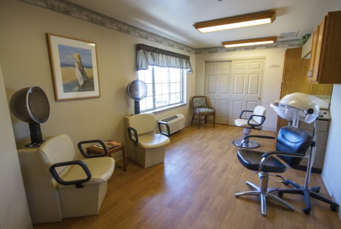 A cozy and well-lit hair salon with chairs for waiting and styling, featuring a wooden floor and a window view.