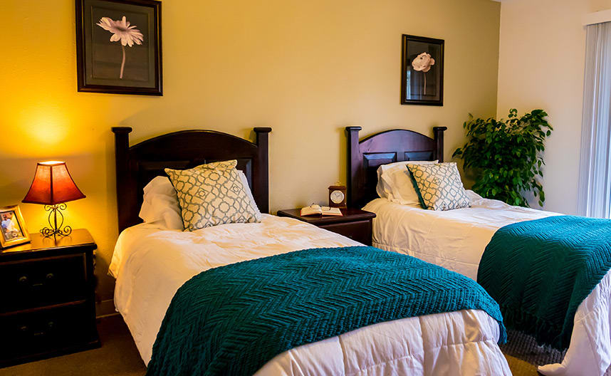 A cozy bedroom with two twin beds, adorned with decorative pillows and teal blankets.