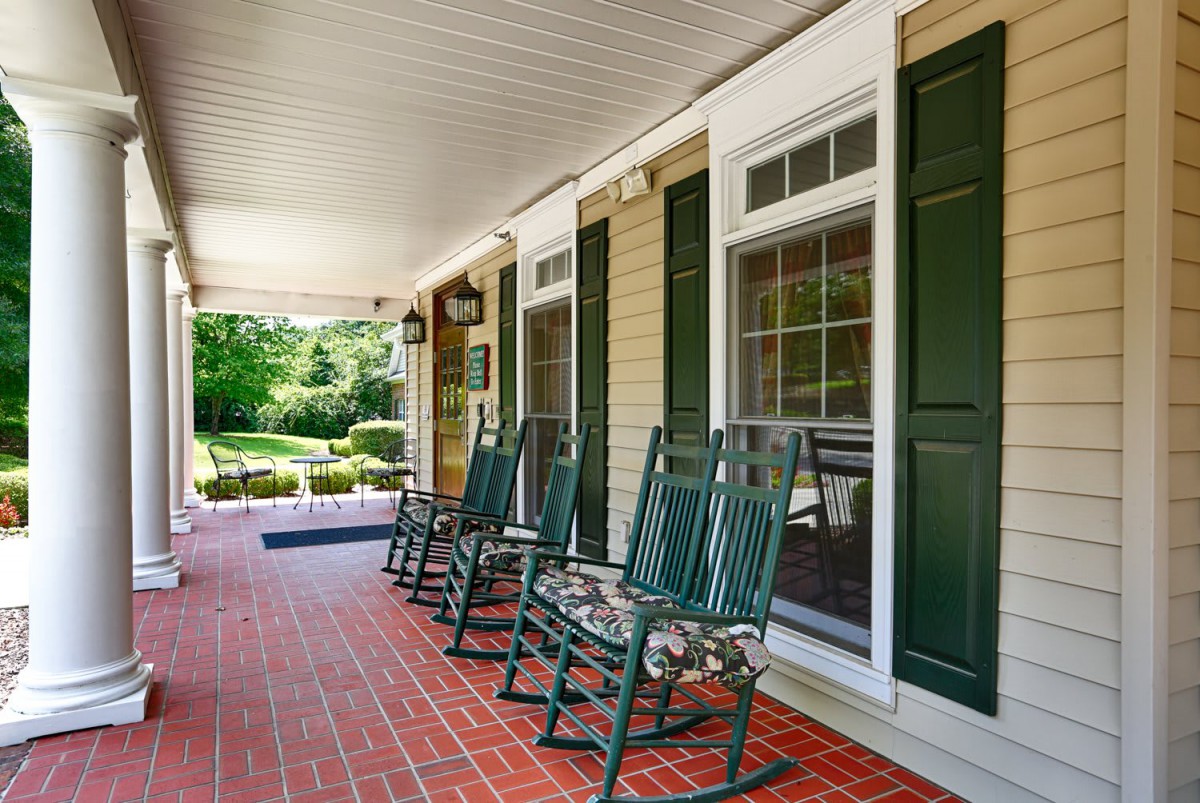 A charming porch with green rocking chairs and a brick floor, featuring windows with green shutters.