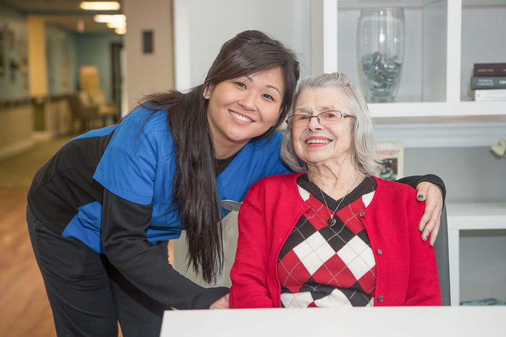 A caregiver smiling next to an elderly woman in a nursing home setting.