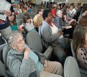 A diverse group of people seated in an audience at an indoor event.