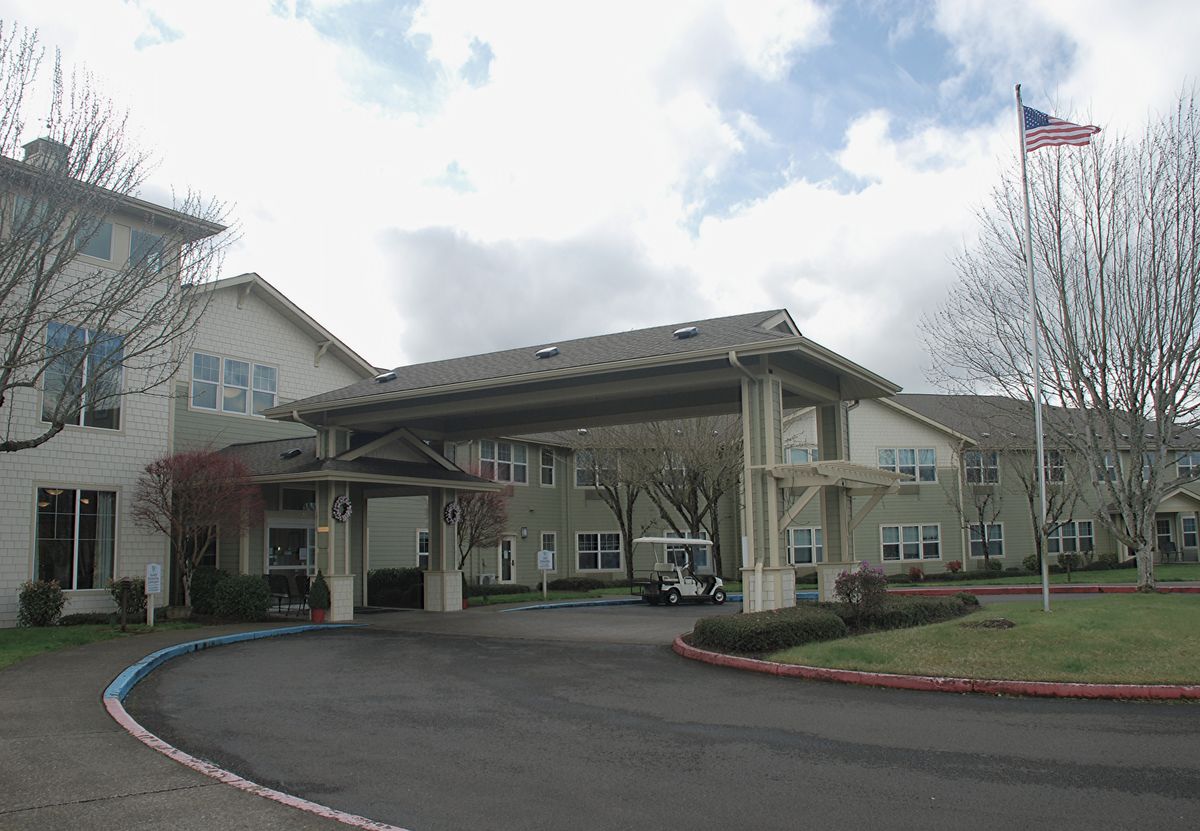 A large building with a covered entrance and a circular driveway under a cloudy sky.