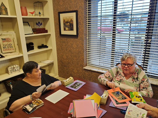 Two individuals engaged in a lively discussion around a table filled with colorful stationery.