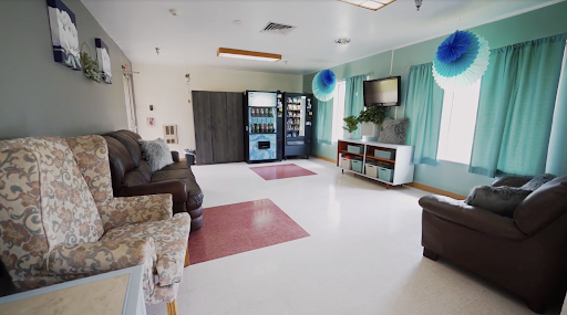 A spacious and well-lit lounge area featuring comfortable seating, a vending machine, and a television.