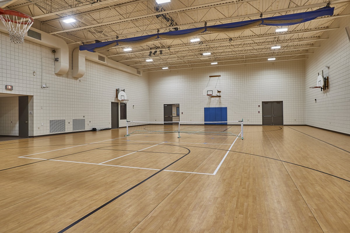 An empty indoor basketball court with wooden flooring and multiple basketball hoops.