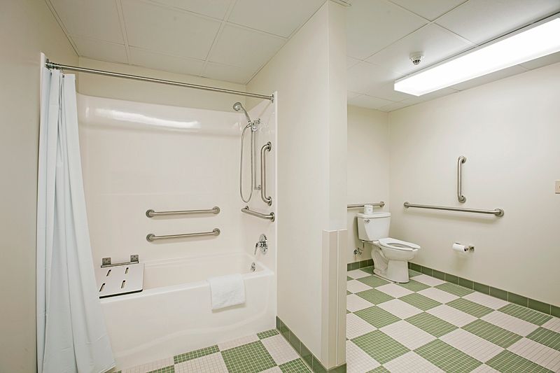 An accessible bathroom featuring a shower with grab bars, a toilet, and a sink, all within a tiled space.