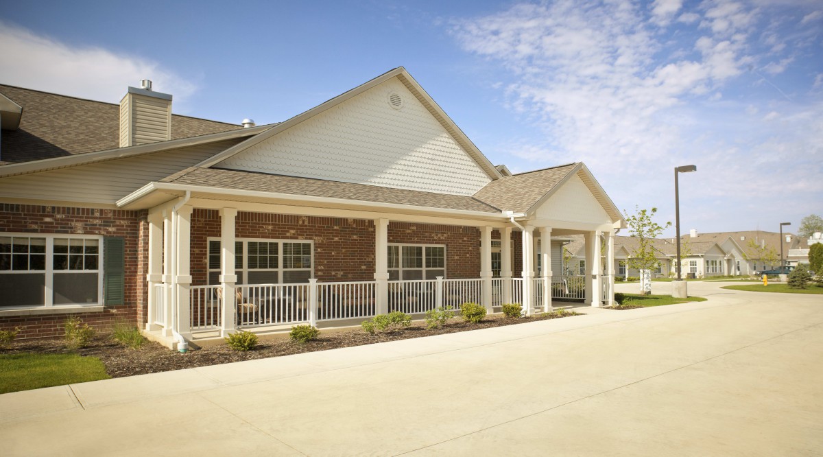 A single-story brick residential house with a porch under a clear blue sky.
