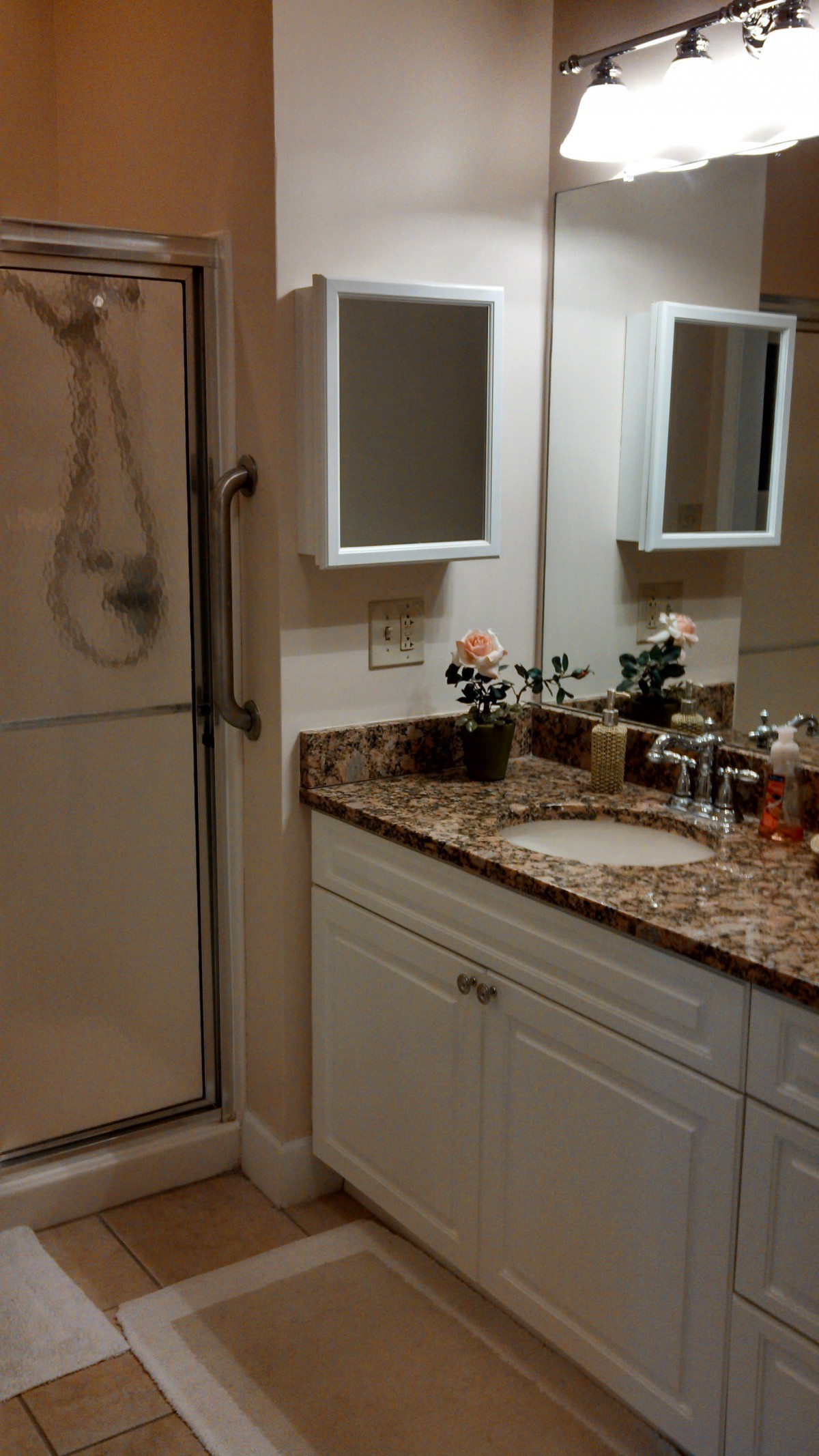 A well-organized bathroom featuring a granite countertop with a sink, mirrors, and a shower enclosure.