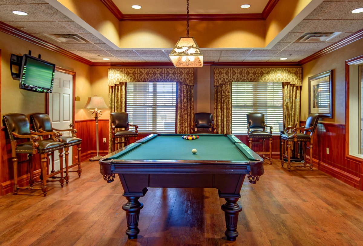 A cozy billiard room featuring a pool table under warm lighting and wood flooring.