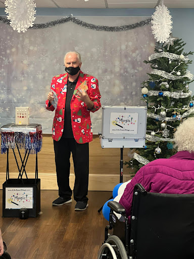 A magician performs for an audience during a holiday-themed event, complete with a Christmas tree in the background.