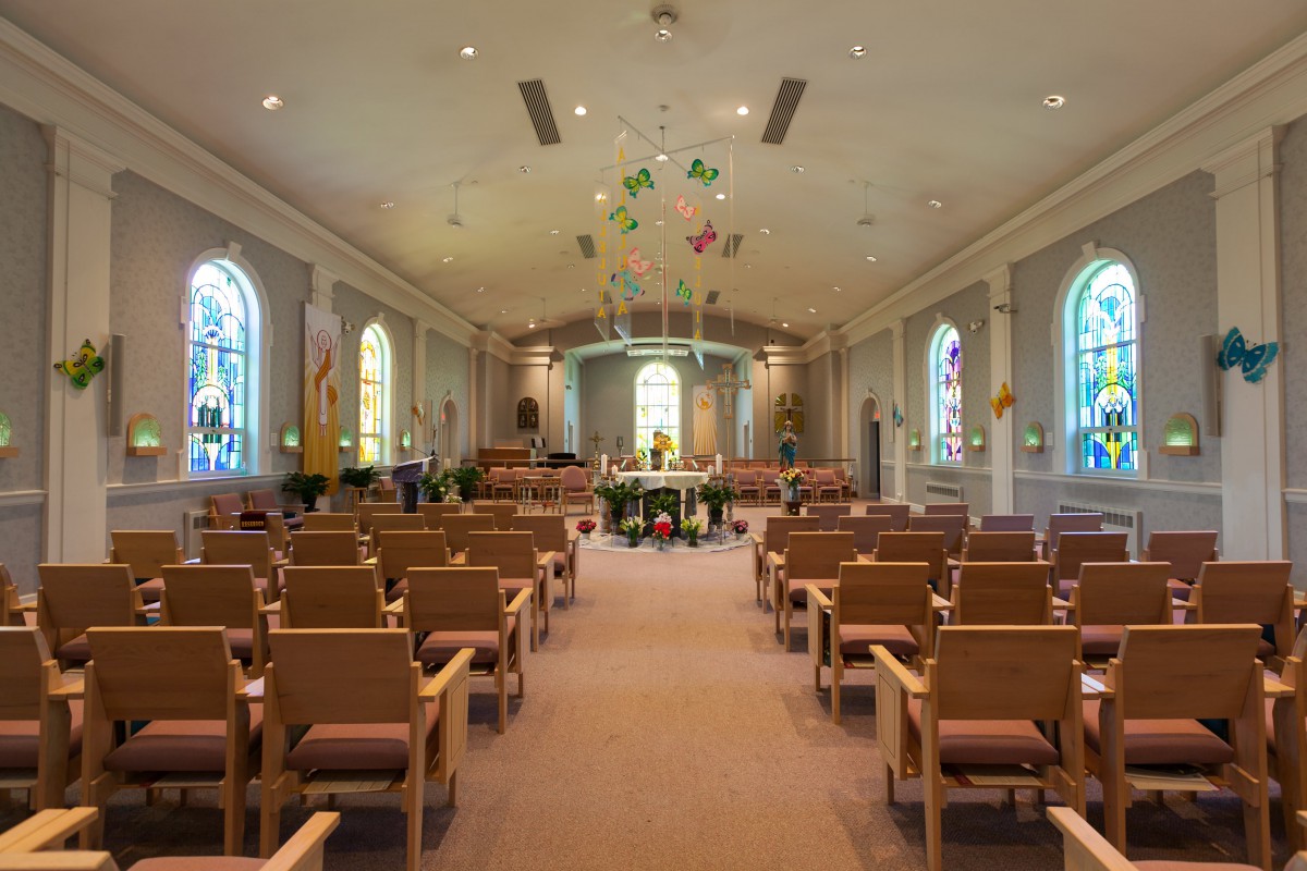 A church interior featuring rows of pews, an altar, and stained glass windows.