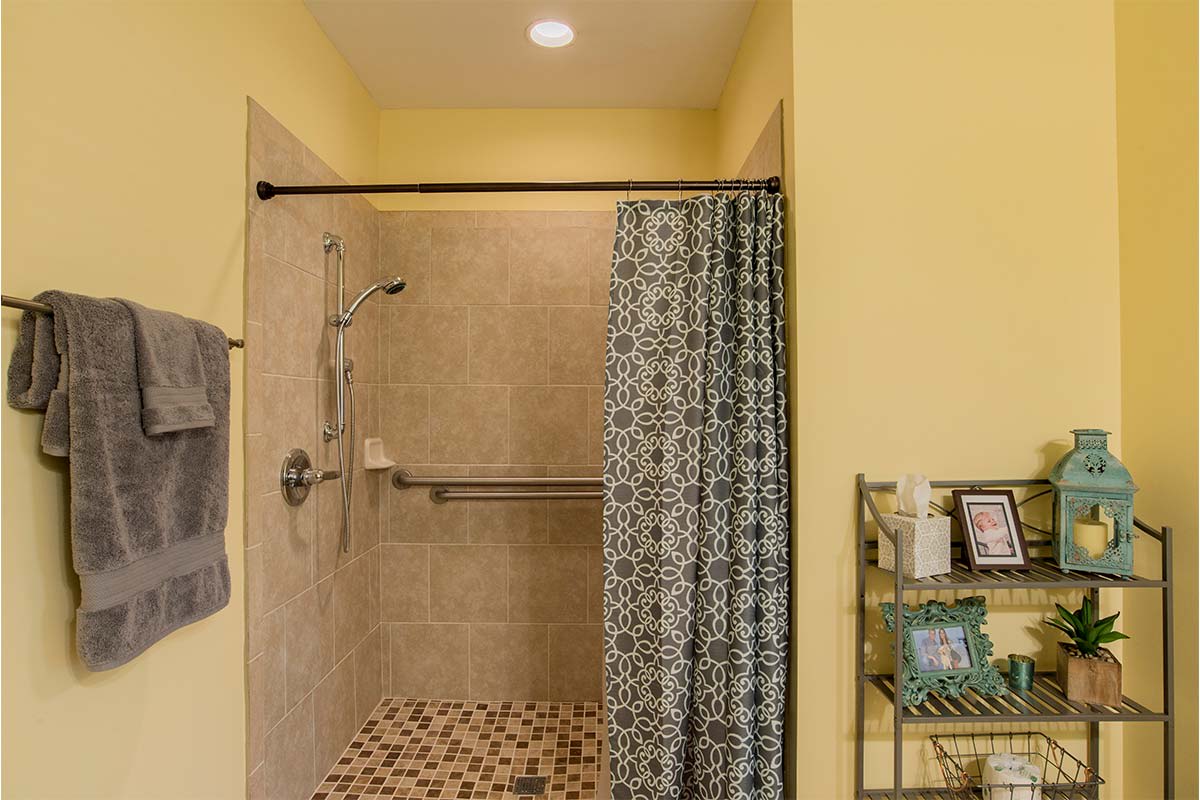 A tiled shower area with a patterned curtain and grab bar, set against yellow walls.