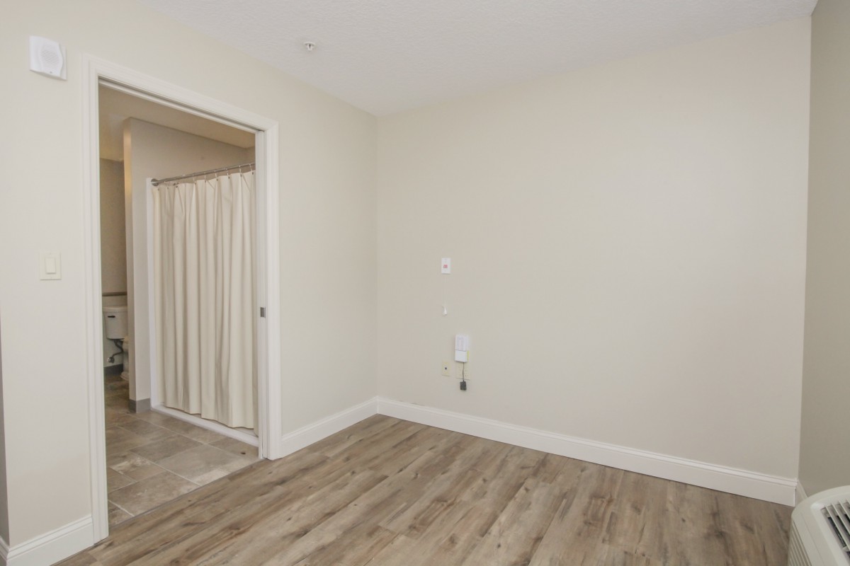 An empty room with wood flooring and white walls, featuring a doorway with a curtain.