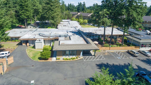 Aerial view of a modern building surrounded by trees and a parking area.