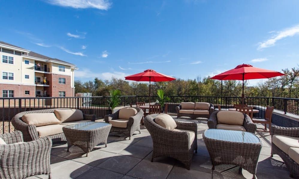 A spacious outdoor patio with wicker furniture and red umbrellas under a clear blue sky.