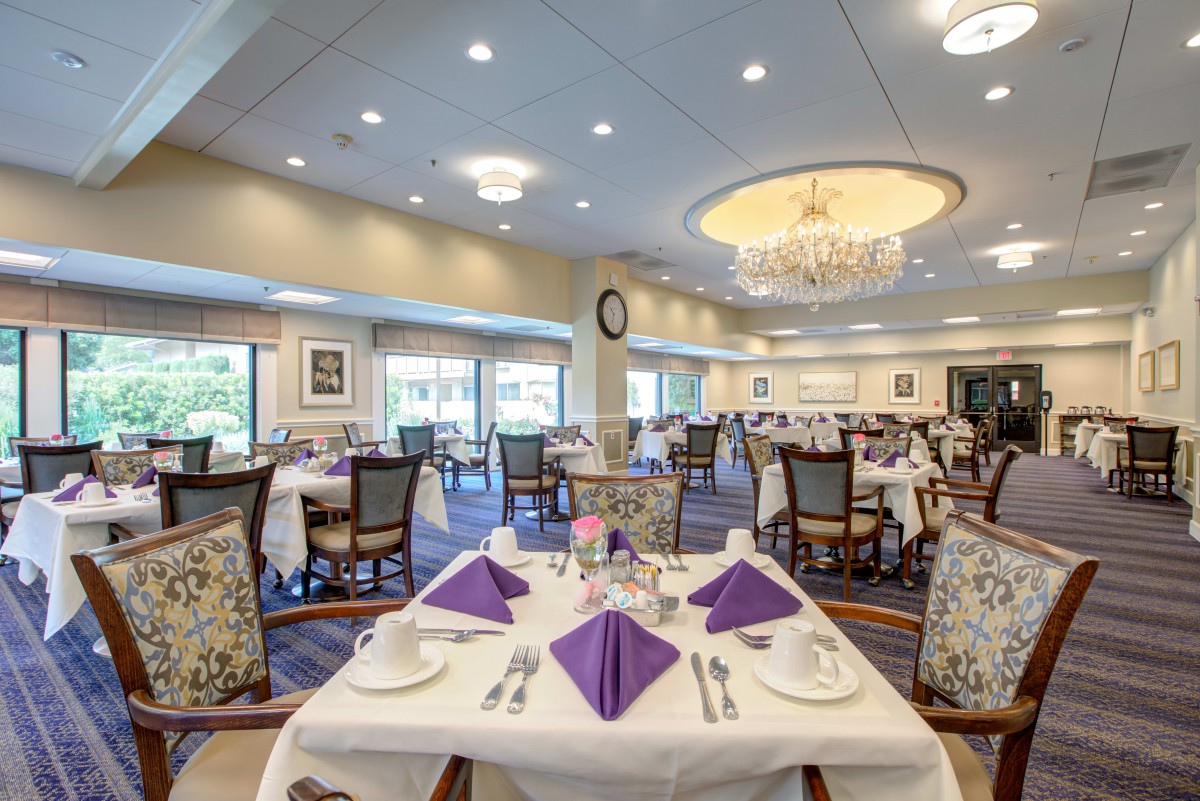 An elegant dining room with beautifully set tables featuring purple napkins and a chandelier.