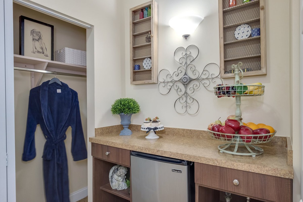 A bathroom vanity area featuring a robe, decorative storage shelves, and a mini-fridge.