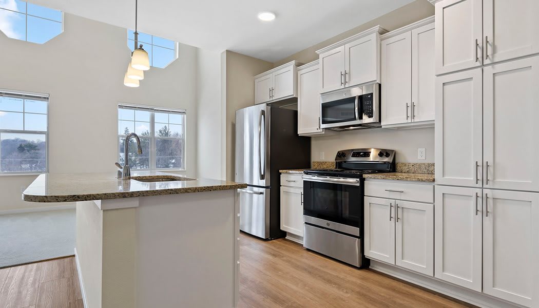 A modern kitchen with white cabinetry and stainless steel appliances, featuring a center island and wood flooring.