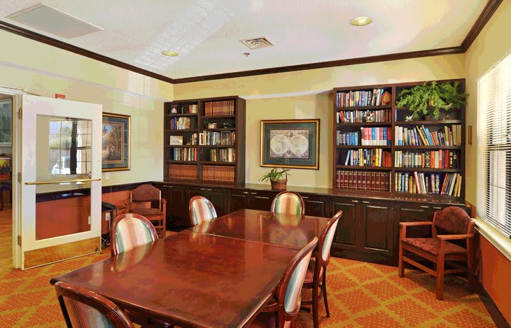 A well-organized library or conference room with wooden bookshelves and a polished meeting table surrounded by chairs.