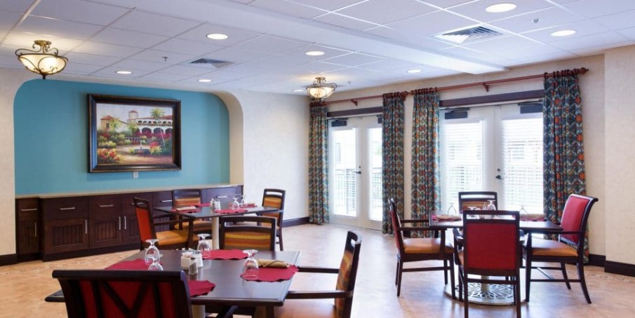 A cozy dining area with neatly arranged tables and chairs, featuring warm lighting and large windows.