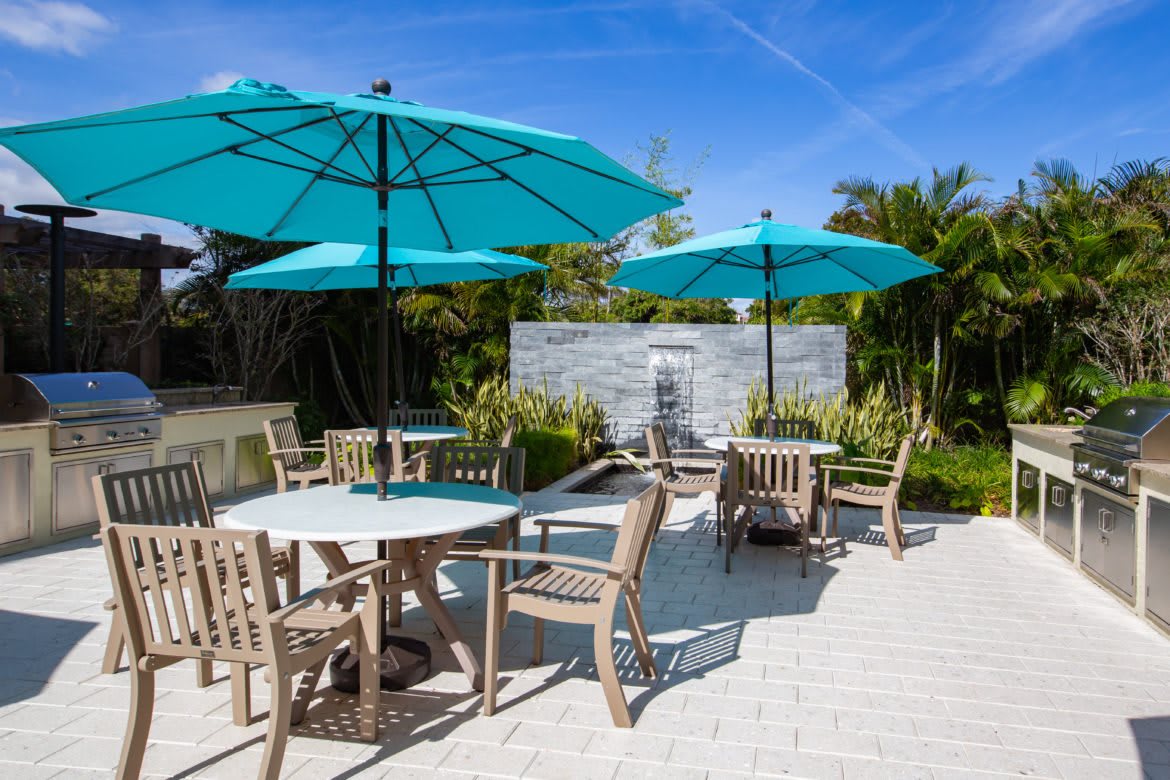 A sunny patio area with tables, chairs, and blue umbrellas.