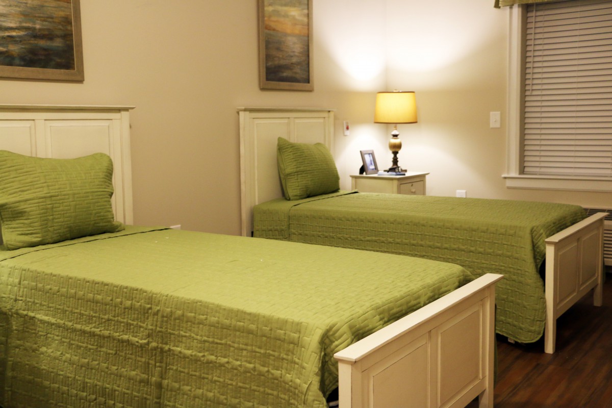 A cozy bedroom featuring twin beds with green bedding and a stylish lampshade on the nightstand.