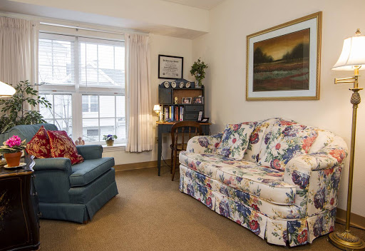 A cozy living room featuring a floral sofa and a blue armchair, complemented by natural light filtering through the windows.