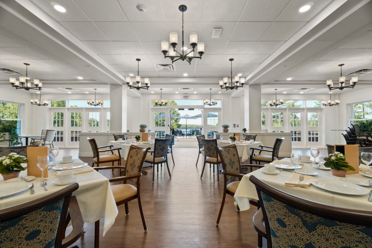 An elegant dining room with neatly arranged tables and chairs, illuminated by chandeliers.