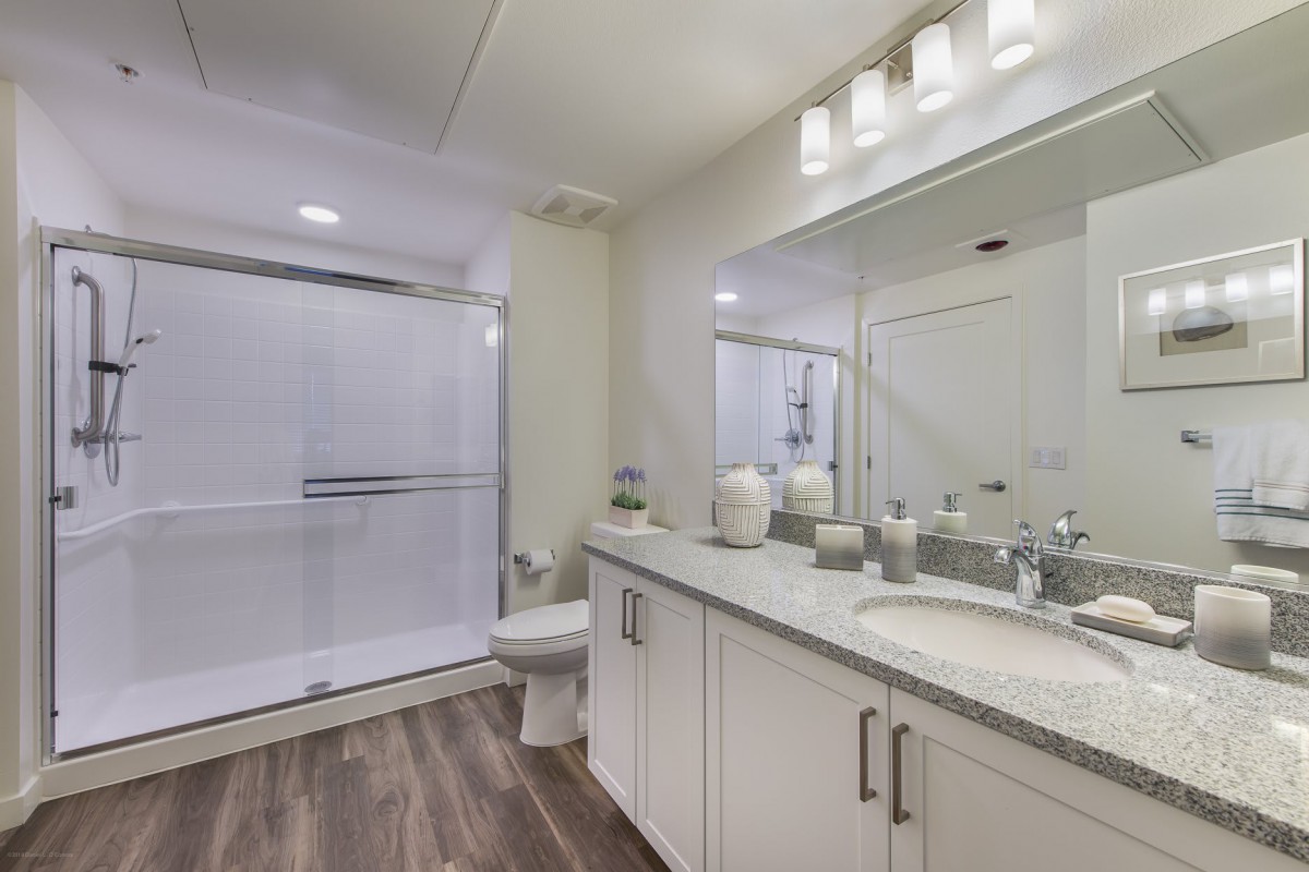 A modern bathroom with a double sink, large mirror, and a glass-enclosed shower.