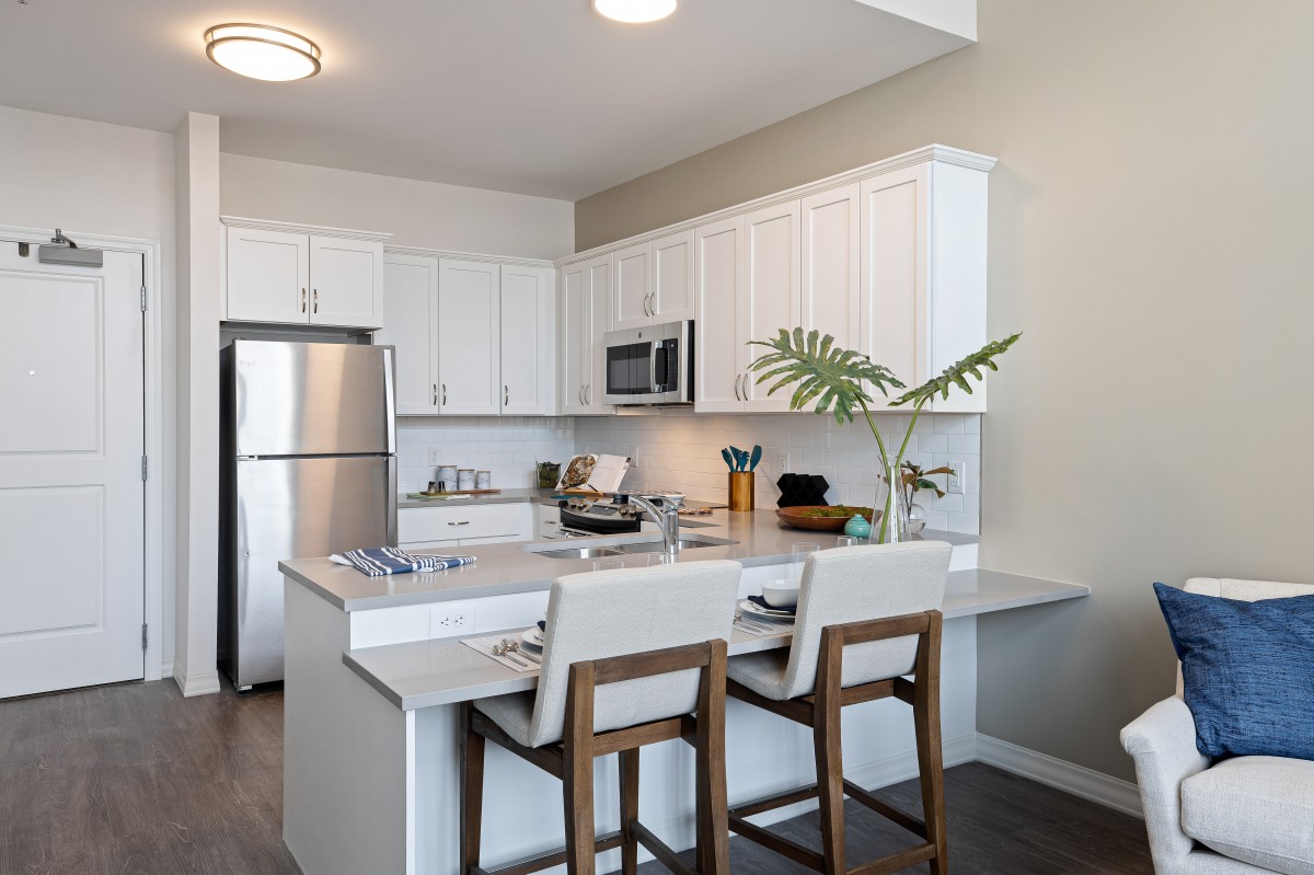 A modern kitchen with white cabinets and a central island, featuring stainless steel appliances and bar stools.