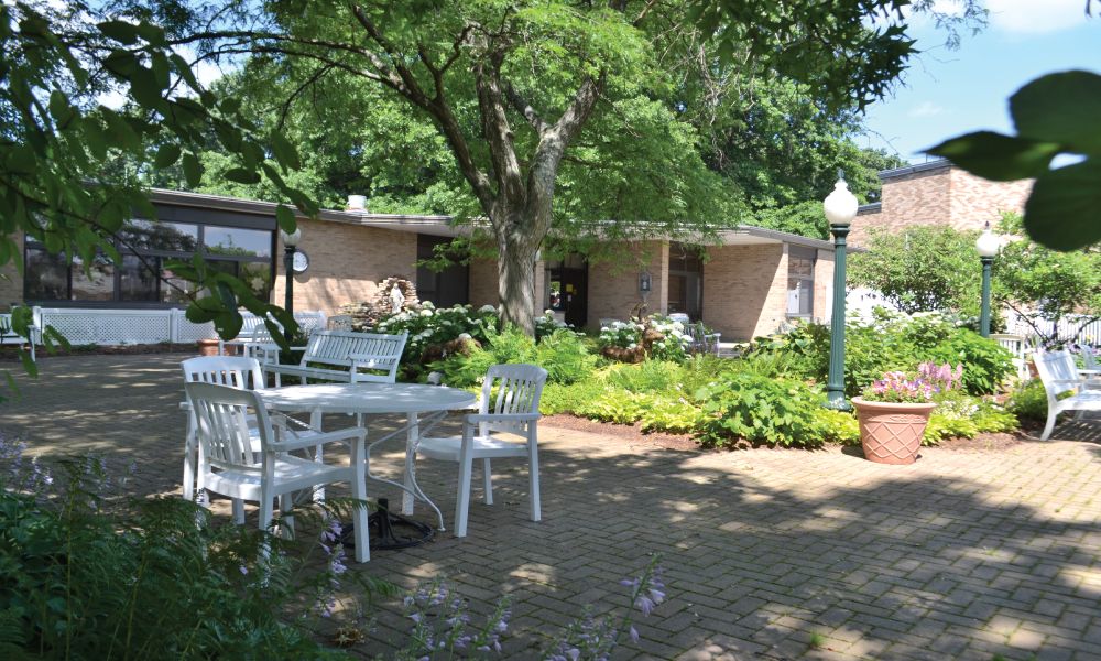 A peaceful garden patio with outdoor furniture and lush greenery on a sunny day.