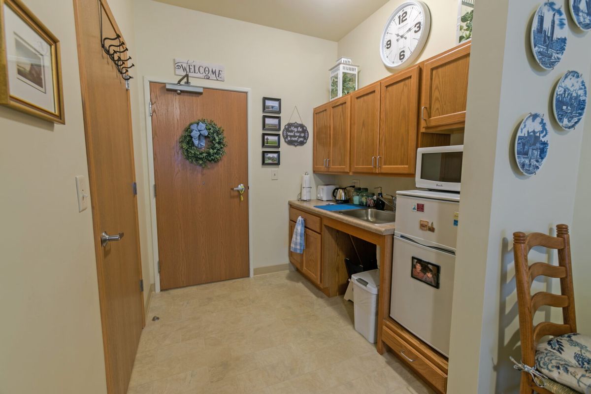 A cozy kitchen with wooden cabinets, a microwave, and refrigerator adorned with decor.