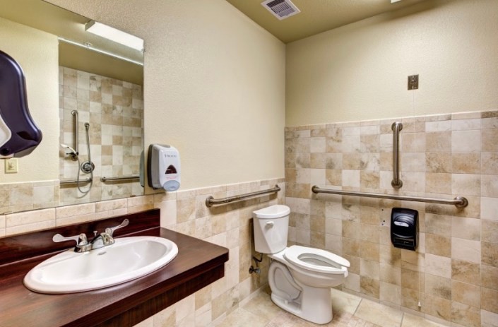 Accessible bathroom with tiled walls and handrails.