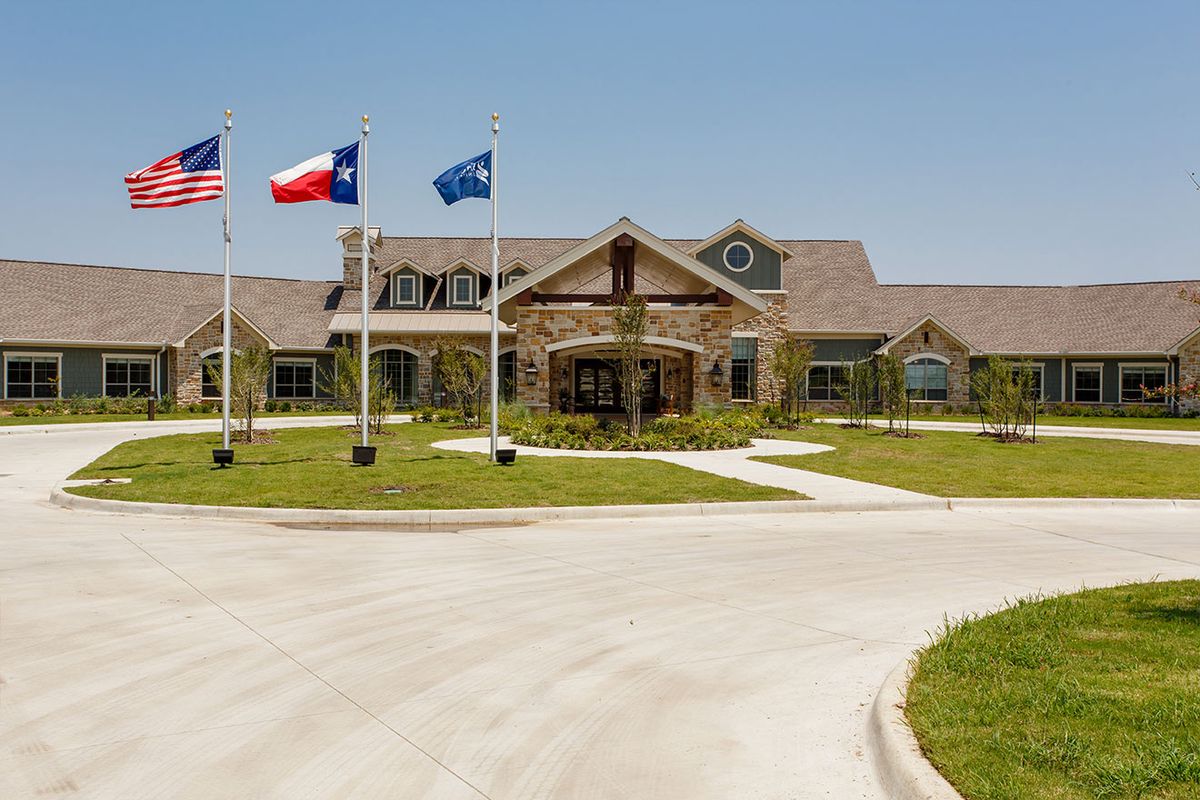 A large building with multiple flags displayed in front, set against a clear blue sky and surrounded by a circular driveway.