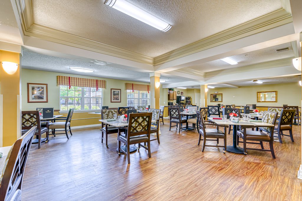 A bright and welcoming dining room with wooden floors, featuring neatly arranged tables and chairs.