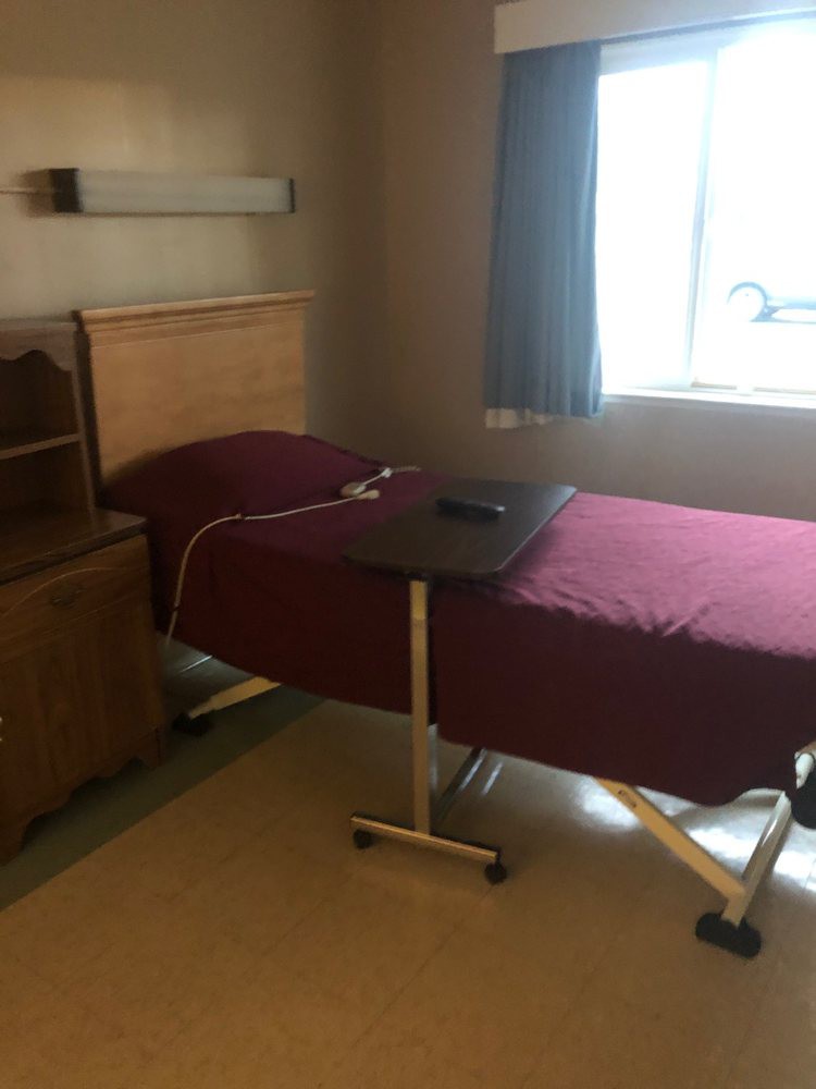 A hospital room with a single bed and a movable overbed table by the window.