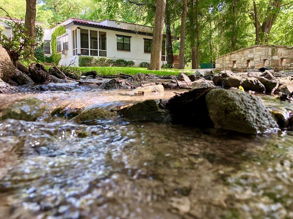 A peaceful stream flows by a house nestled in the forest.