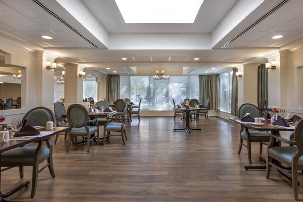 A spacious dining room with elegant decor, featuring multiple tables and chairs, large windows, and wooden flooring.