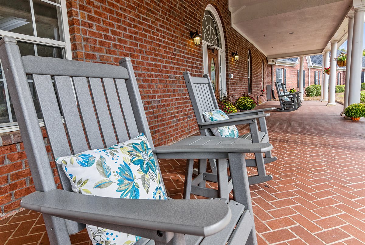 A cozy porch with rocking chairs and decorative pillows against a brick wall.